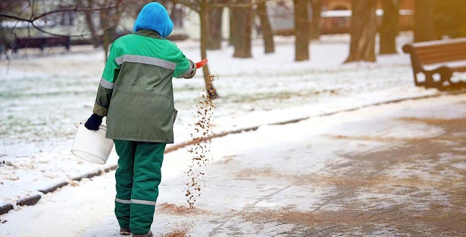 Winterdienst Mitarbeiter streut Streusalz auf Gehweg zur Vermeidung von Glätte